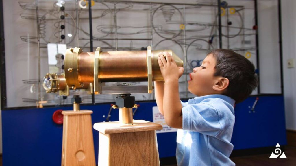 little kid looking through telescope at museum