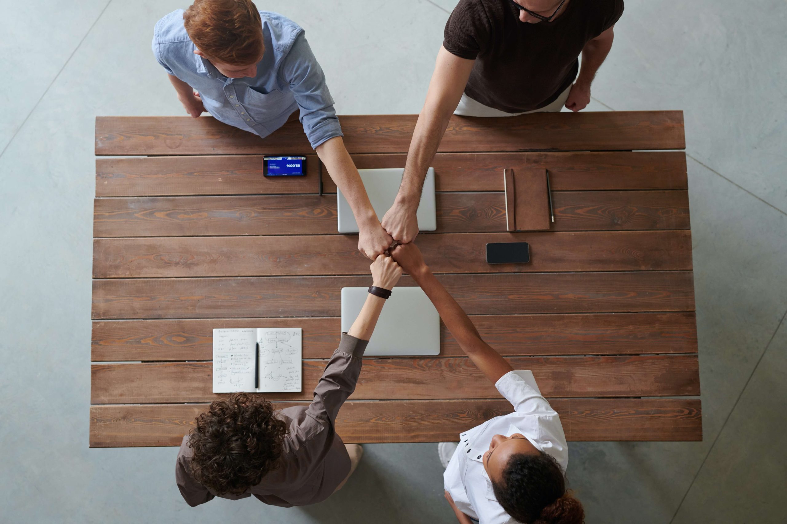 four people touching hands over a table