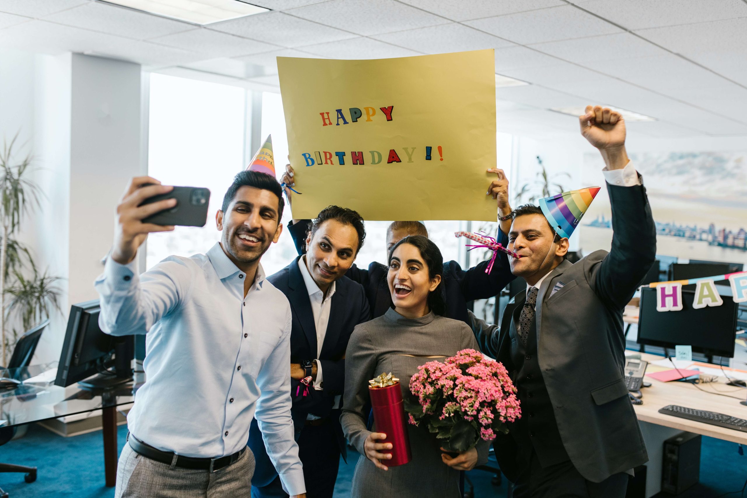 team members wearing birthday hats and holding a sign that says happy birthday