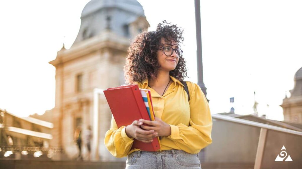 person standing with college textbook in front of college building