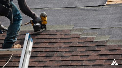 person stapling shingles into roof